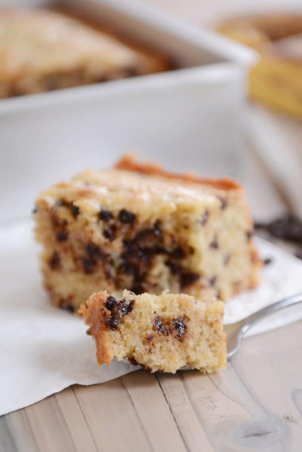 A fork taking a bite out of a piece of banana chocolate chip cake.