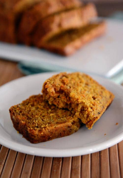 A white plate with two slices of banana carrot bread and the rest of the loaf behind it. 