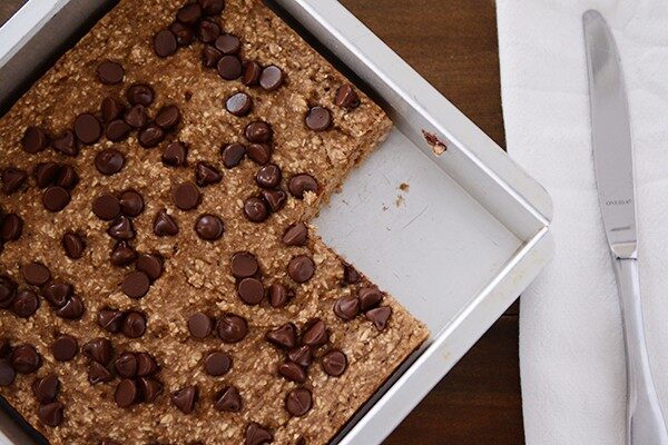 Top view of a square pan of banana oat chocolate chip bars with a piece cut out.