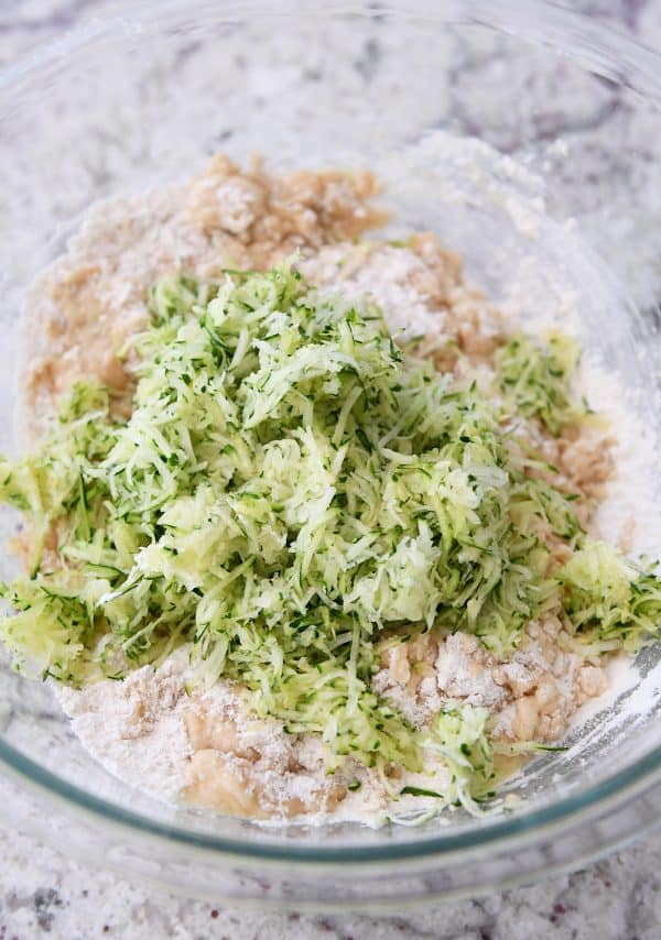 Glass bowl with zucchini banana bread batter; shredded zucchini on top.