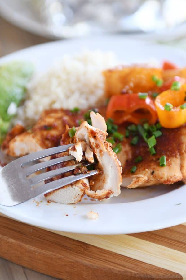 Fork taking a bite of BBQ hawaiian chicken off a plate of chicken, peppers, and rice.