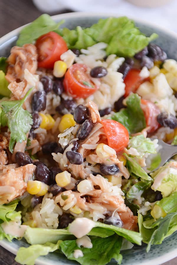 A chicken, rice, black bean, and veggie mixture served over lettuce in a white bowl.