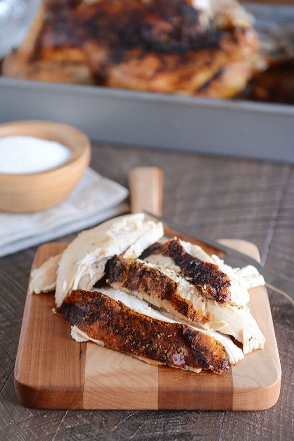 Four big pieces of honey roast chicken on a small wooden cutting board.