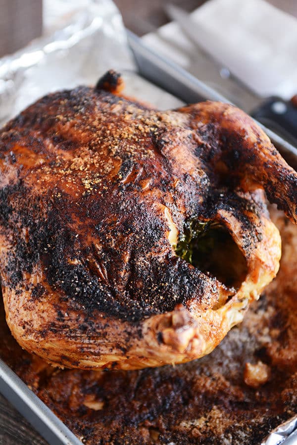 A dark roasted whole honey chicken on a tinfoil-lined cookie sheet.