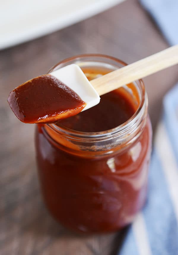 A mason jar full of BBQ sauce with a rubber spatula with sauce on it laying on the top.