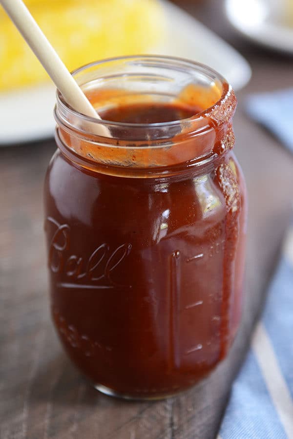 A mason jar full of BBQ sauce, with a drip coming down the side and a wooden spoon in the jar.