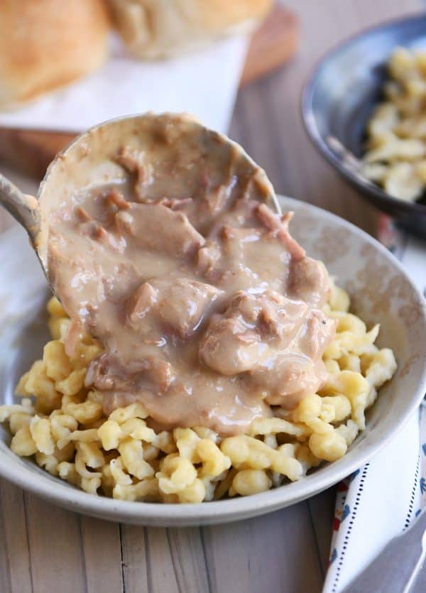 Pouring slow cooker beef stroganoff over spaetzle noodles.