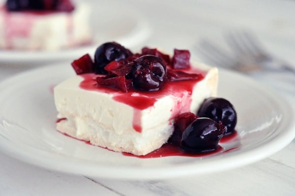 A white plate with a square of meringue dessert with berries on top.