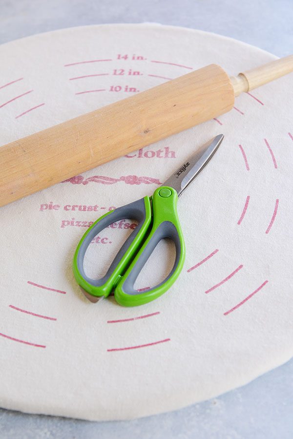Scissors and a wooden rolling pin on top of a pie crust pastry cloth.