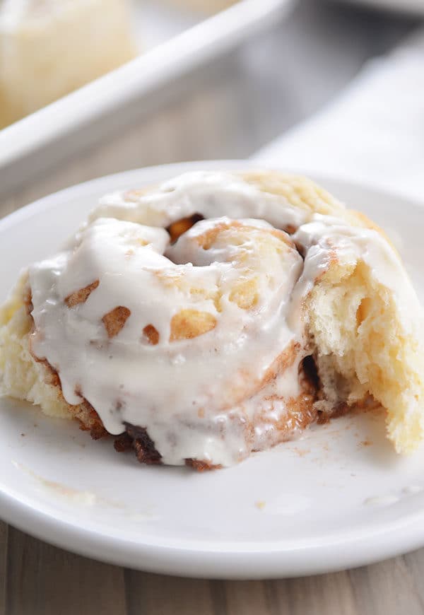 A frosted cinnamon roll with a piece ripped off on a white plate.