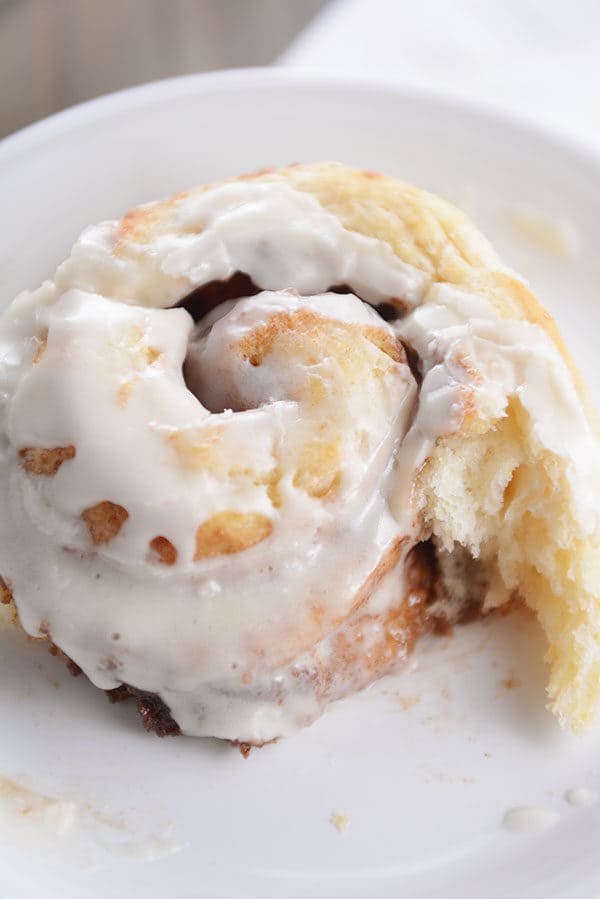 A frosted cinnamon roll with a bite taken out on a white plate.