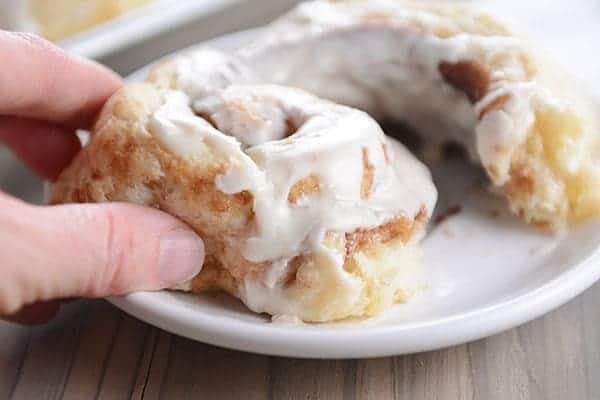 A hand pulling a bite off of a frosted cinnamon roll. 