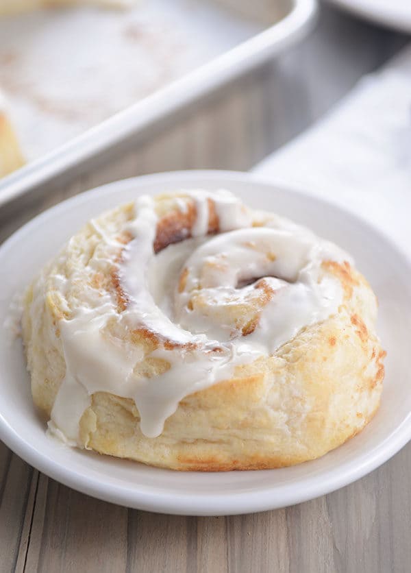 A frosted cinnamon roll on a small round white plate.