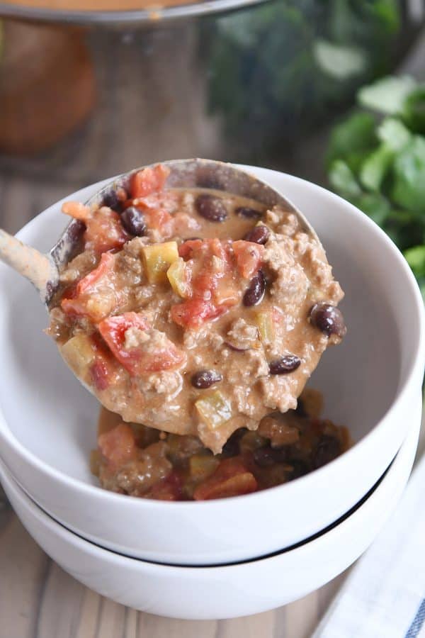 Ladling in creamy black bean taco soup to white bowl.