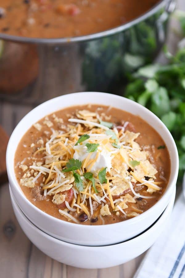 Top view of a bowl of creamy black bean taco soup topped with crushed tortillas chips, sour cream, and cheese.