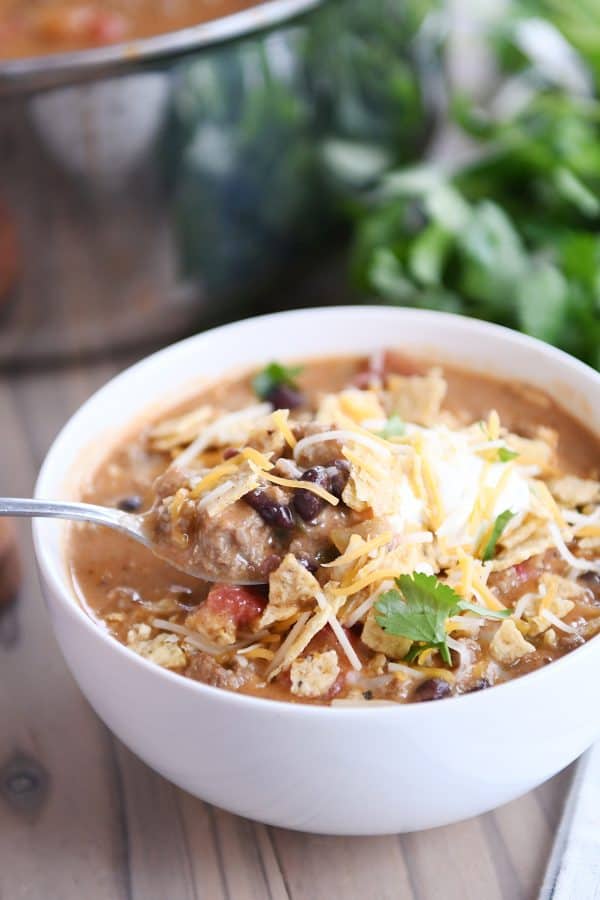 A spoon taking a bite of creamy black bean taco soup with sour cream and cheese on top out of the bowl. 