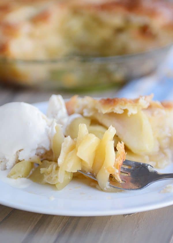 Slice of apple pie and a scoop of vanilla ice cream on a white plate.