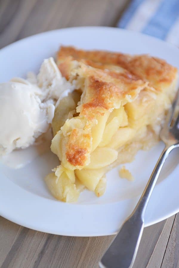 Slice of apple pie with a scoop of vanilla ice cream next to it on a white plate.