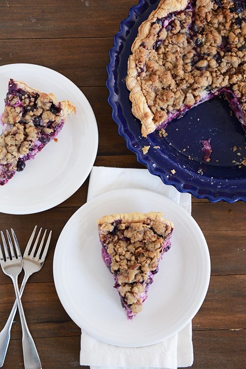 Top view of two white plates with slices of blueberry custard pie and the rest of the pie behind them.. 