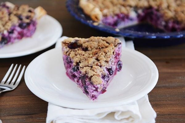 A slice of streusel-topped blueberry custard pie on a white plate.
