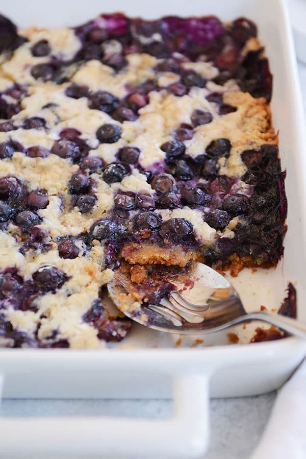 A large white dish of blueberry cake with a scoop taken out of the side. 