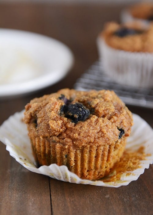 A blueberry pumpkin muffin on a white muffin liner. 