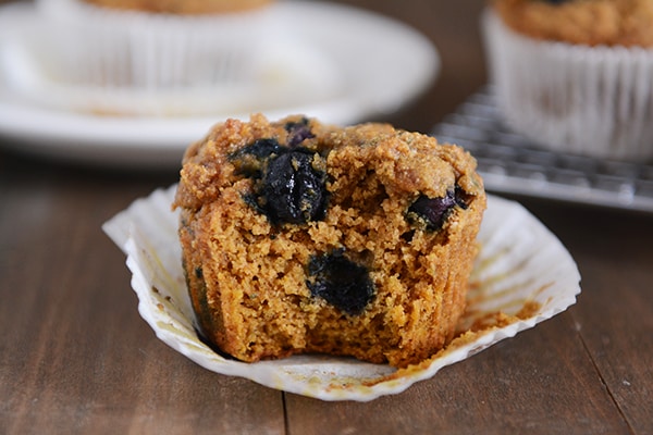 A blueberry pumpkin muffin with a bite taken out on a white liner. 