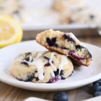 Blueberry muffin cookies on white plate with top cookie broken in half.