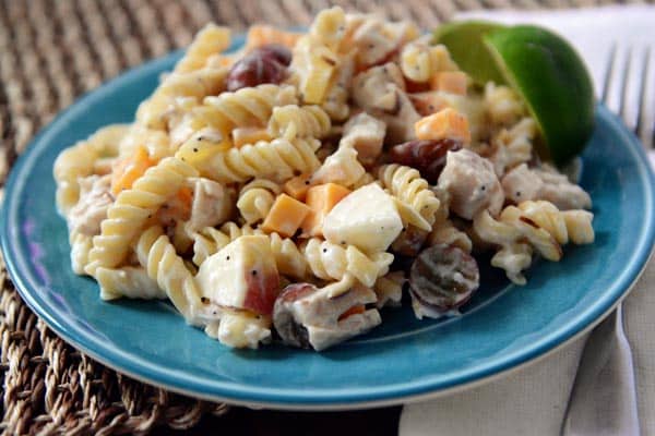 Blue plate with creamy pasta chicken salad with cubes of apple, grapes, and cheddar cheese.