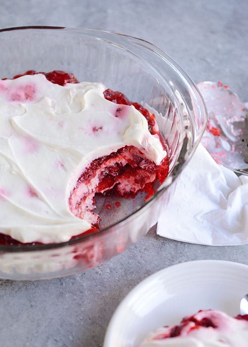 A glass bowl of layered raspberry Jello dessert with a scoop taken out.