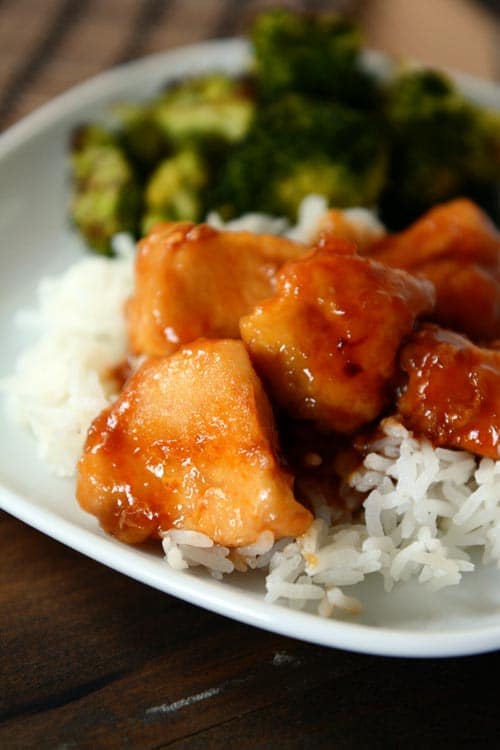 Bourbon sauce covered chicken on white rice on a white plate.