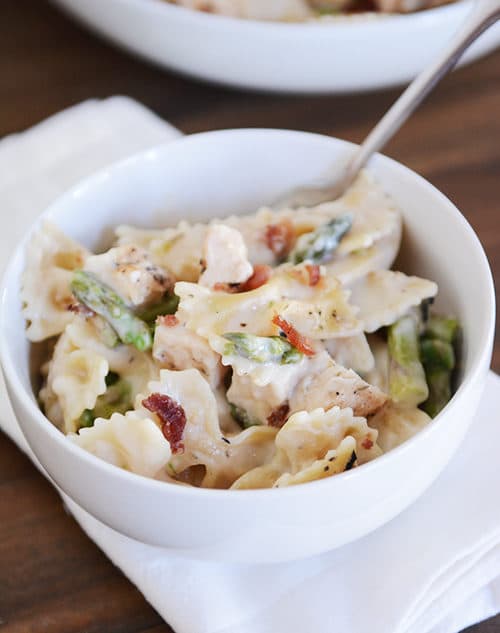 White bowl of creamy bowtie pasta with chopped asparagus.