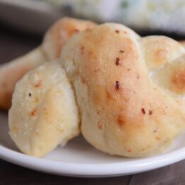 Two Parmesan breadstick knots on white plate.