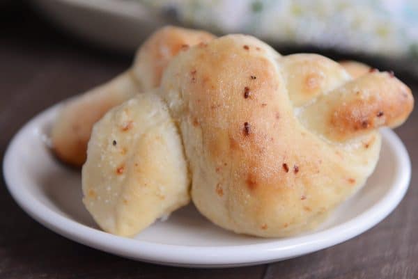 Two Parmesan breadstick knots on white plate.