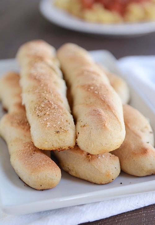 A white plate with five cooked breadsticks.