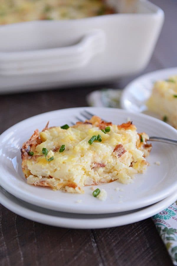 A piece of cheesy egg and hash brown casserole on a white plate, with a bite taken out.