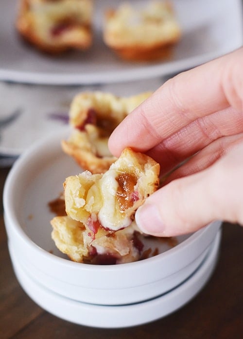 A puff pastry brie bite broken in half with other bites in a bowl below it.