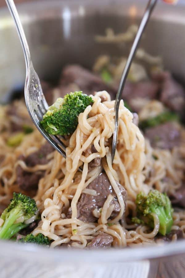 Lifting up ramen noodles with beef and broccoli out of pot with one fork.