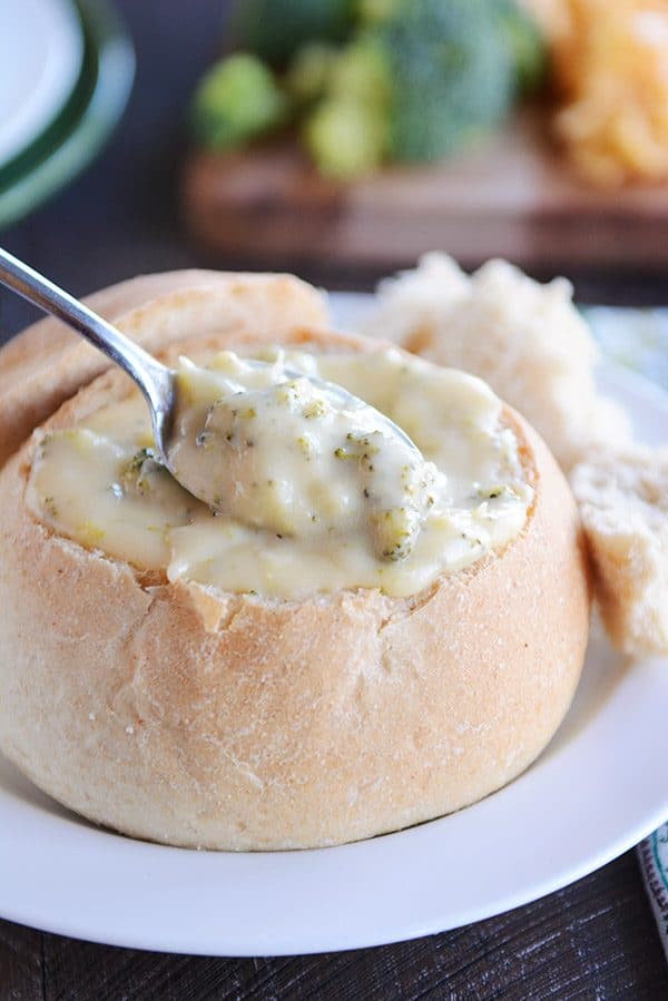 Spoon dipping into bread bowl filled with broccoli cheese soup.