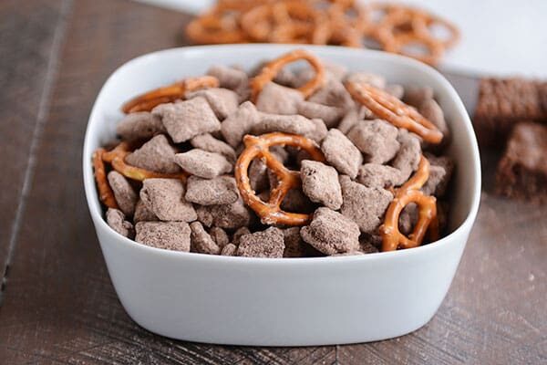 Chocolate muddy buddies and pretzels in a white bowl.