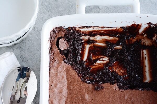 a white ceramic dish full of brownie pudding, with the front third of the dish scooped out and already eaten. 