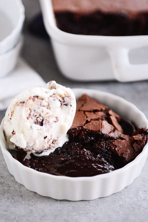 A white ramekin full of brownie pudding with a scoop of ice cream on top.