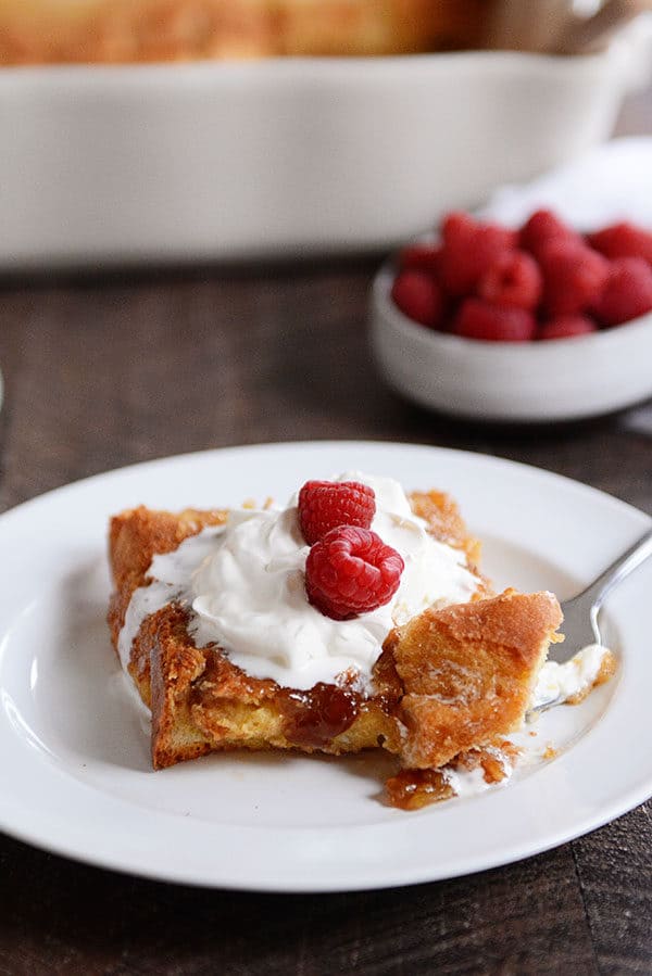 A fork taking a bite out of apiece of creme brulee french toast topped with whipped cream and raspberries.