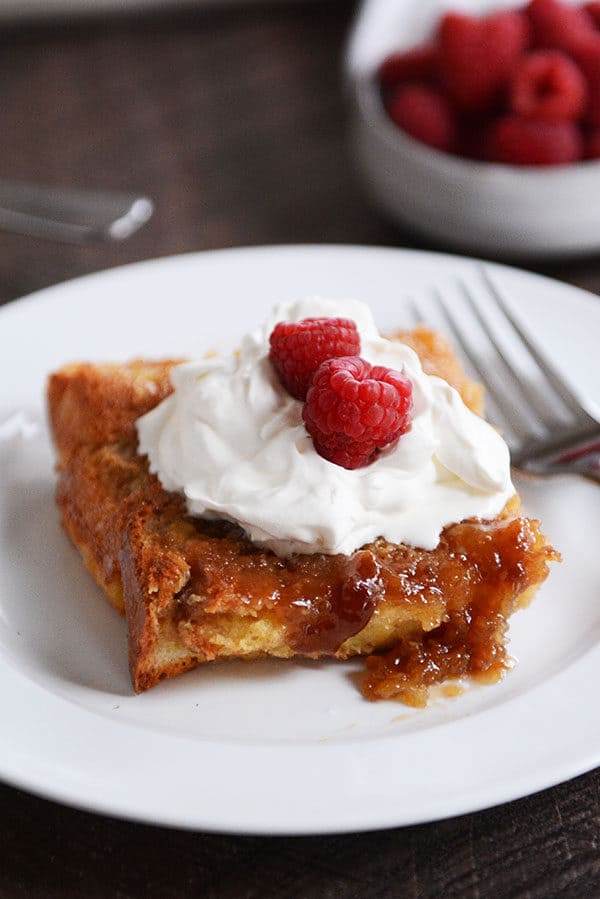 A piece of creme brulee french toast topped with whipped cream and rasperries.