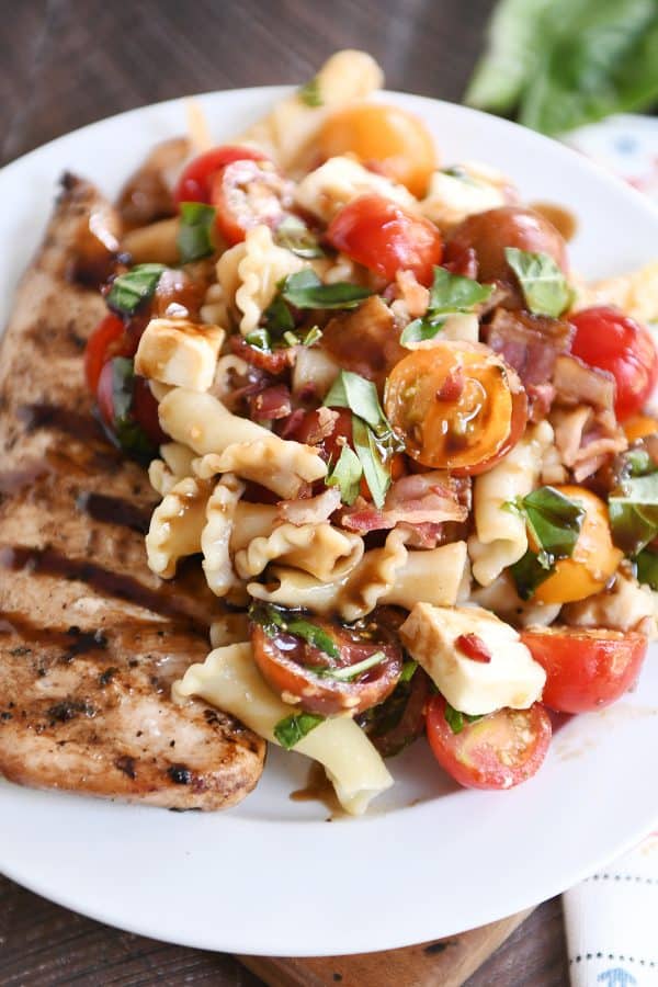 Close up of bruschetta chicken and bacon pasta on white plate.