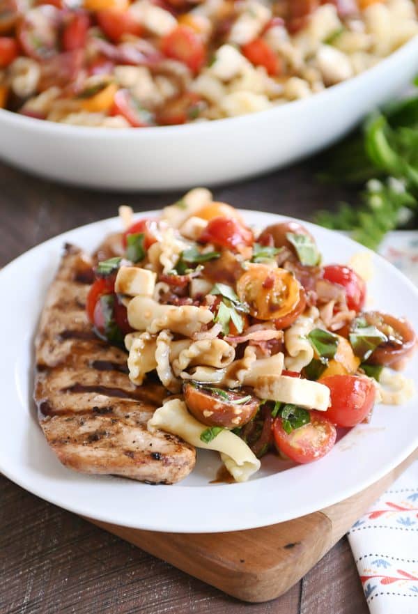 Bruschetta chicken and bacon pasta on white plate and bamboo board.