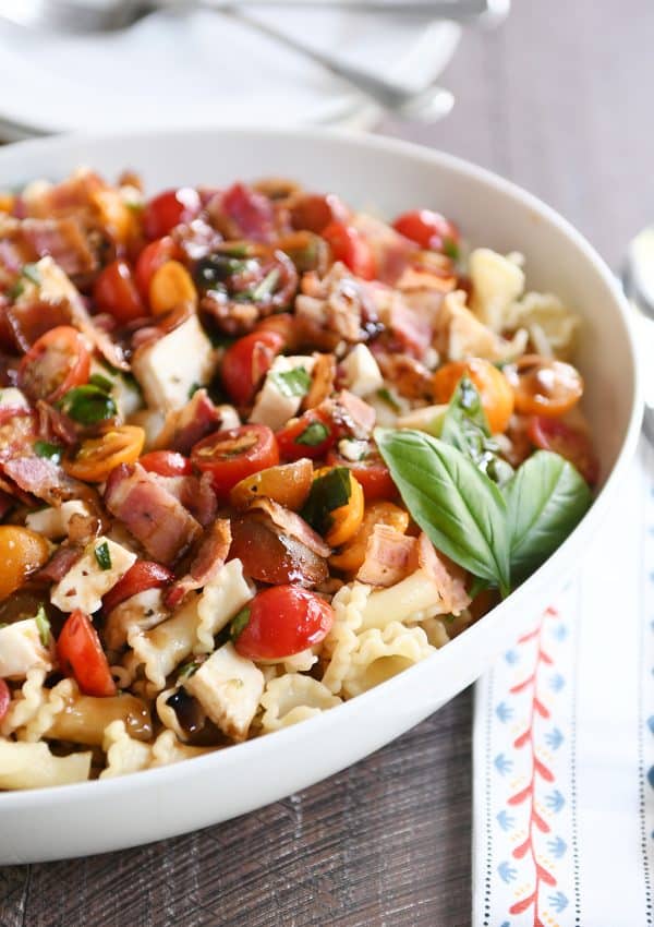 Bruschetta chicken and bacon pasta in large white serving bowl with fresh basil.
