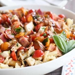 Bruschetta chicken and bacon pasta in large white serving bowl with fresh basil.