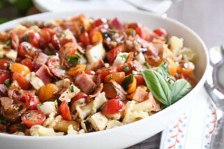 Bruschetta chicken and bacon pasta in large white serving bowl with fresh basil.