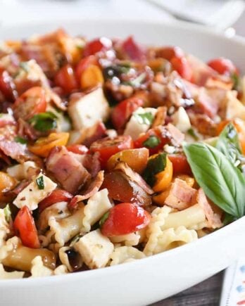 Bruschetta chicken and bacon pasta in large white serving bowl with fresh basil.